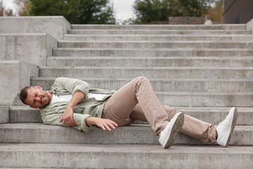 Man with injured arm on stairs outdoors after fall. Dangerous accident