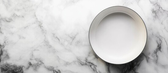 Empty white ceramic plate on a marble surface with copy space for text or design elements.