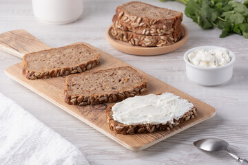 Slices of whole grain bread topped with cream cheese on a wooden cutting board in a cozy kitchen setting