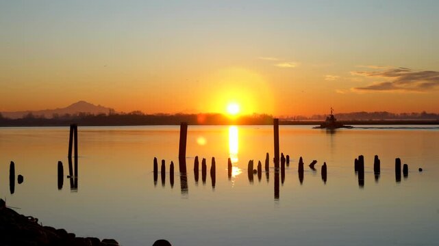 Fraser River Tugboat Sunrise 4K UHD. A tugboat travels upriver in front of the Cascade mountains on the Fraser River. British Columbia, Canada. 4K, UHD.
