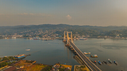 Aerial photo at sunset from the Kendari Bay Bridge which is the icon of the city. Aerial panorama at dusk of the suspension bridge that connects the two lands and divides the bay