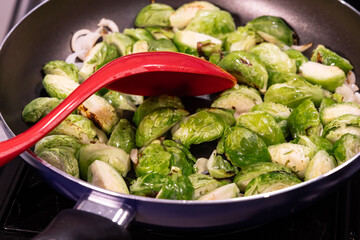 Closeup of a saucepan or frying pan of cut up Brussels sprouts with a large mixing spoon