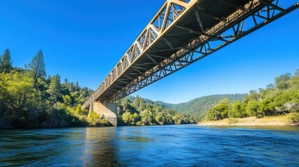 Fototapeta premium Low-Angle Shot of a Modern Steel Bridge Spanning Over a River Beneath a Clear Blue Sky, Symbolizing the Achievement of Civil Engineering Design and Innovation