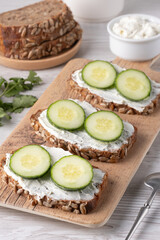 Slices of whole grain bread topped with cream cheese and fresh cucumber arranged beautifully at a rustic wooden table