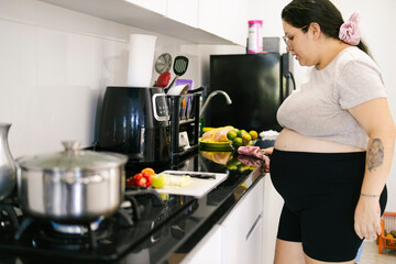 Pregnant colombian woman cooking a family meal in a modern kitchen