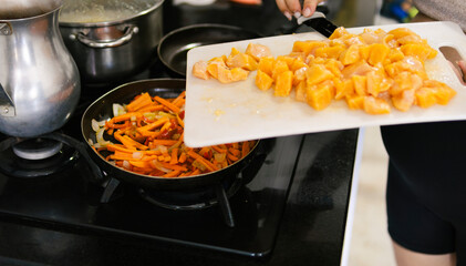 Woman adding chicken to frying pan with sauteed vegetables