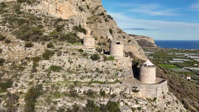 Aerial video shot of three ruined windmills on the famous Red Rock above the town of Leonidio in Peloponnese, Greece