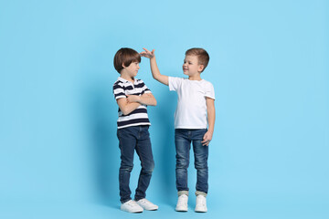 Cute brothers comparing their height on light blue background