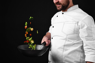 Professional chef mixing vegetables in wok on black background, closeup