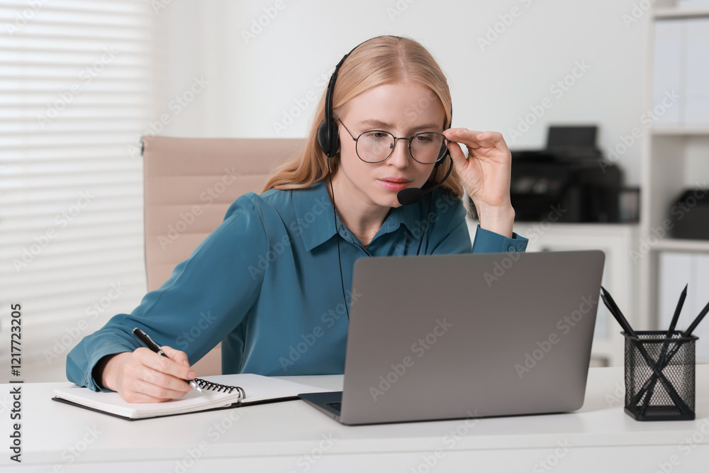 Poster interpreter in headset taking notes while working with laptop at table indoors