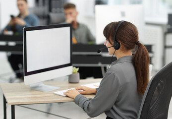 Saleswoman talking to client via headset at desk in office