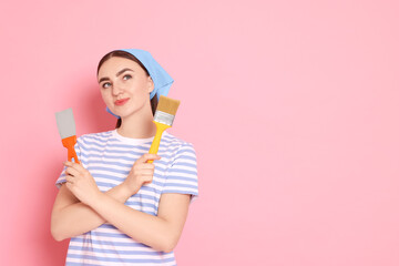 Portrait of young decorator with putty knife and brush on pink background, space for text