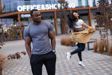 Muscular man poses, woman twirls. A man stands confidently while a woman playfully twirls in front...
