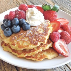 Pancake Heaven: A delightful stack of fluffy pancakes, adorned with fresh strawberries, blueberries, raspberries, and a dollop of whipped cream, creating a mouthwatering breakfast scene.
