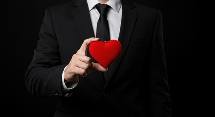 A person from the waist up dressed in a formal black suit with a white shirt and the individual is holding a red velvet heart shape object in his right hand seems proposing for valentine's day