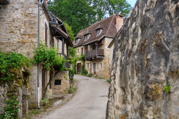 View of a small street with old houses in the medieval village of Carennac in Lot Occitanie Southern France under a blue sky with clouds in summer. 