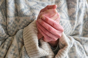 Closeup of the red cold hands of a caucasian woman trying to get wam in a thick knitted sweater in...
