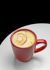 Ginger tea in a red mug with an apple chip garnish, placed on a white table with a black background. A healthy and warming beverage, perfect for cafe or restaurant menus.