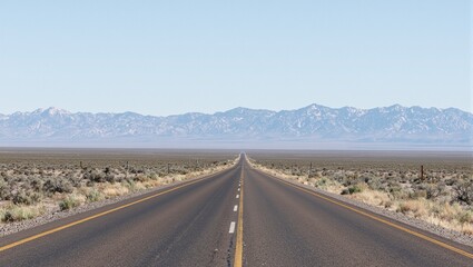 Fototapeta premium Scenic desert road with scrubby vegetation and distant mountains under clear blue sky