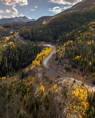 A stunning aerial view of a winding mountain road surrounded by autumn colors and evergreen trees, capturing the breathtaking seasonal beauty of a natural landscape.