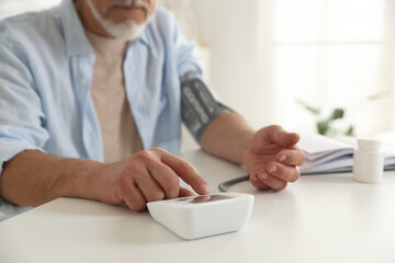 Senior man measuring blood pressure at table indoors, closeup