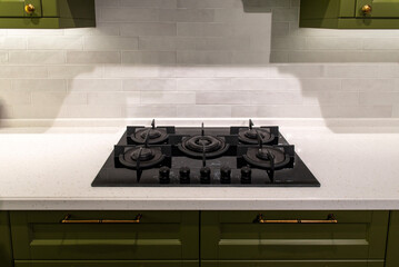 Black glass gas stove on stone countertop in green kitchen