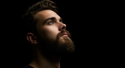 A trendy man with a sharp beard looks up with intensity, creating a bold contrast against the dark background.
