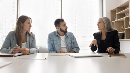 Three business partners participate in briefing or negotiations hold by mature businesswoman, company boss, team leader make speech, express point of view, planning cooperation, engaging in teamwork