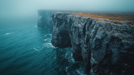 Dramatic coastal cliffs meet a foggy seascape at dawn near the shoreline