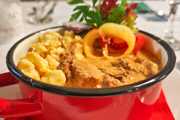 A hearty serving of traditional beef stew with rich creamy sauce, paired with golden dumplings in a vibrant red enamel pot.