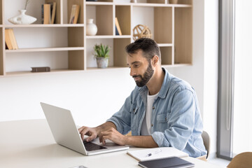 Young Hispanic businessman working online on project using laptop, answers on e-mail, lead business...