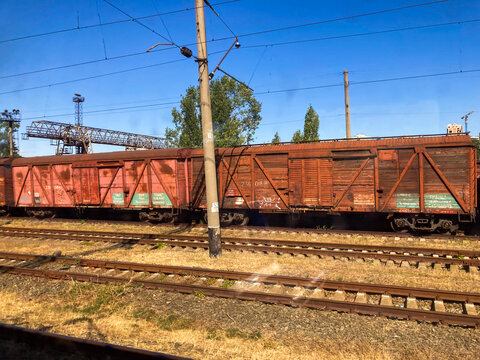 A candid photograph shows a stopped freight train on twin tracks, surrounded by natural greenery and an overhead power line The wagons are red, used for bulk cargo like - Kyiv, Ukraine 06-02-2024