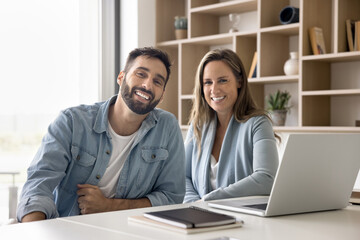 Portrait of two successful businesspeople posing together seated at workplace table. Successful,...