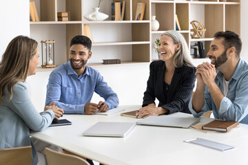 Happy workmates engaged in positive conversation gather in boardroom, joking, sharing creative...