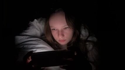 A Portrait of a Young Attractive Woman Playing Game on Smartphone in the Bed at Night teenage girl dark under the blanket - Powered by Adobe