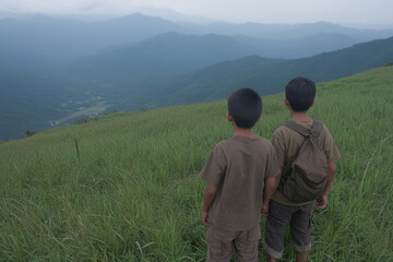 Naklejka premium Two young boys are standing in a grassy field looking out over the mountains