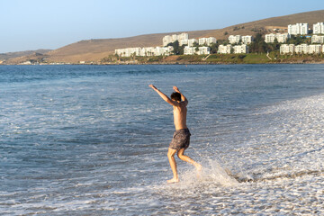 A young man enthusiastically leaping into the sea to swim, with the warm hues of the sunset...