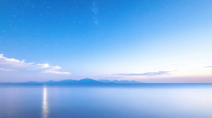 Fototapeta premium Tranquil ocean reflecting starry night sky with distant mountains and soft clouds at twilight
