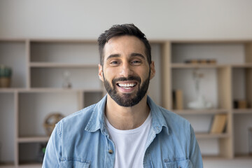 Happy Hispanic millennial 30s man posing alone indoors. Head shot portrait of successful...
