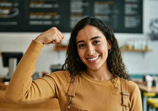 Smiling barista flexing her bicep, demonstrating strength and confidence in her workplace