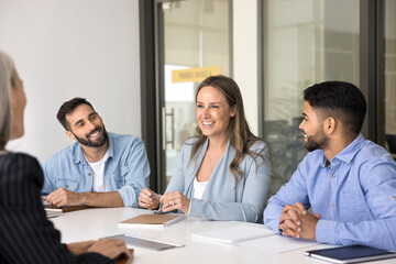 Diverse office employees take part in seminar led by mature 40s businesslady, laughing together engaged in friendly, informal conversation seated at conference table in office. Companionship, teamwork