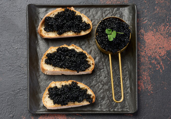 Sandwiches with black caviar served on a black plate, top view