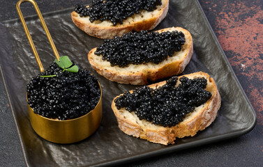Sandwiches with black caviar served on a wooden board