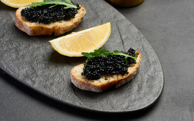 Sandwiches with black sturgeon caviar on a black plate and lemon slices