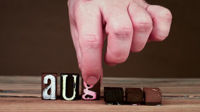 August. Spelling word using wooden alphabet blocks