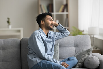 Fototapeta premium Pleasant thoughts. Happy millennial single man relax at living room sitting on sofa at comfortable pose look at window imagine successful life create plans for future enjoy spending leisure time alone