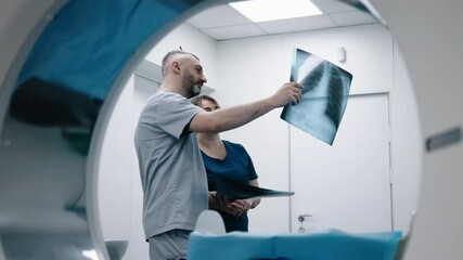 Two doctors in an MRI or CT room reviewing images and discussing the results. The concept of teamwork and precise analysis for diagnosing conditions of organs and the bone system.