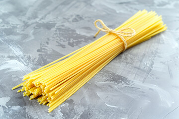 A bundle of uncooked, yellow pasta tied with twine rests on a textured gray surface. Concept of rustic culinary preparation, simplicity.