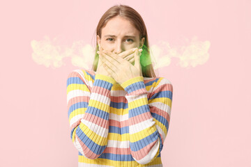 Young woman feeling bad smell on pink background