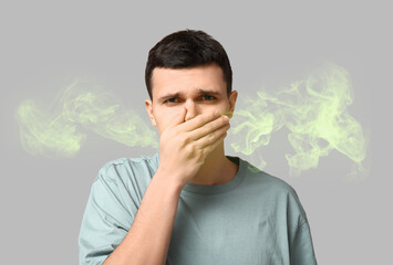 Handsome young man feeling bad smell on grey background